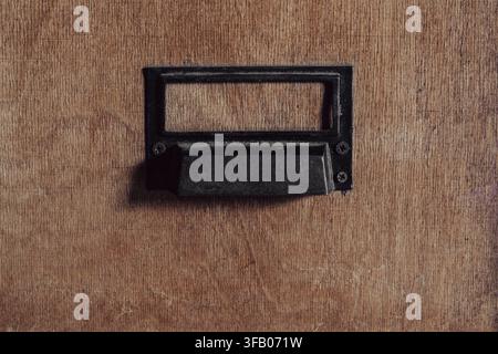 Vintage wooden drawer with empty metal label holder. Close up of an old wooden library file cabinet drawer with a black metal handle and empty index c Stock Photo
