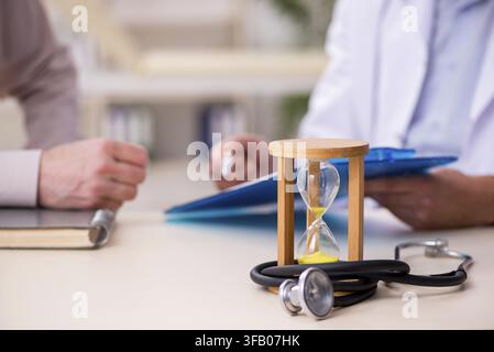 Old male patient visits young doctor in time management concept Stock Photo