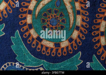 Paisley pattern on textured fabric background, close up. Macro view of colorful traditional paisley ornament printed on dark blue rough linen textile Stock Photo