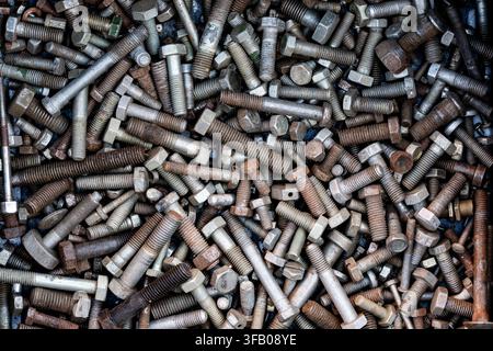 Full frame background of mixed old metal bolts and screws, close up. Top view macro shot of chaotic pile of various old used metallic bolts screws and Stock Photo