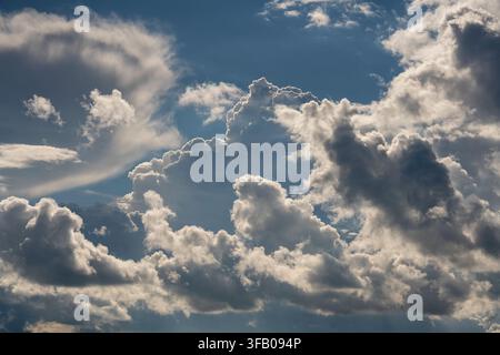Dramatic fluffy cumulus clouds on blue summer sky. Beautiful contrast view of bright white and dark storm cumulus clouds gathering in blue sky during Stock Photo