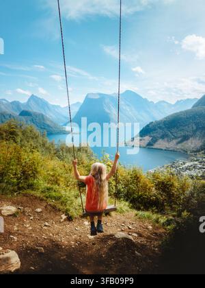 Child girl swinging with fjord and mountains view family travel in Norway, kid having fun playing outdoor active vacations hiking adventure tour in Su Stock Photo