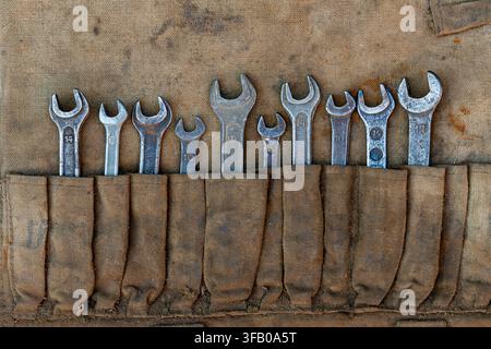 Vintage open end wrenches set in canvas tool roll organizer. Close up old used metallic spanners in dirty fabric pouch toolkit for car repair mechanic Stock Photo