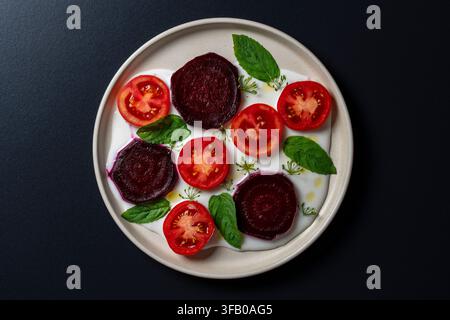 Top view of fresh gourmet salad with sliced red tomatoes roasted beetroot fresh mint leaves and creamy white yogurt sauce served on ceramic plate over Stock Photo