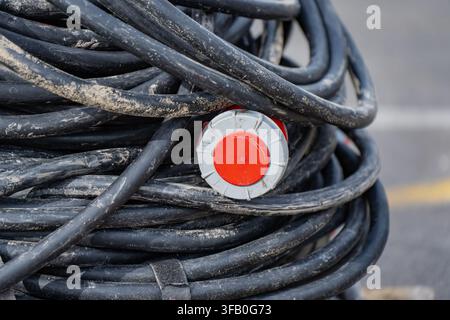 Industrial three-phase power cable roll with red heavy-duty plug connector for temporary electrical distribution on job sites Stock Photo