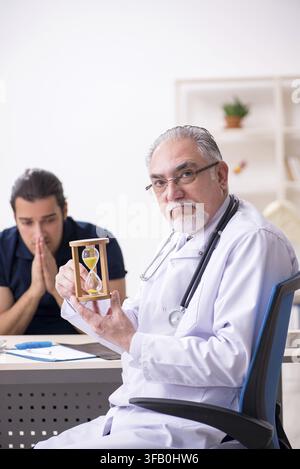 Young male patient visits elderly doctor in time management concept Stock Photo