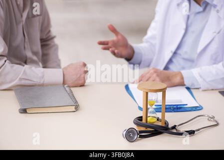 Old male patient visits young doctor in time management concept Stock Photo