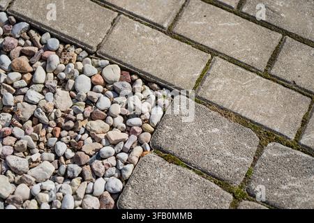 Interlocking concrete paving stones meeting a bed of decorative garden pebbles and gravel landscape edging in a modern courtyard Stock Photo