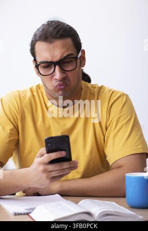 Young student using cell phone while preparing for exams Stock Photo