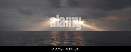 Sun rays breaking through clouds over a calm ocean at sunset, creating a dramatic and serene atmosphere.. Amalfi Coast, Italy Stock Photo