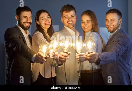 Smiling business team holding glowing light bulbs, symbolizing new ideas, innovation and teamwork. Stock Photo