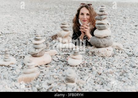 Woman beach rock stacks lying on a pebble shore with stone cairns for harmony and relaxation during a seaside vacation Stock Photo