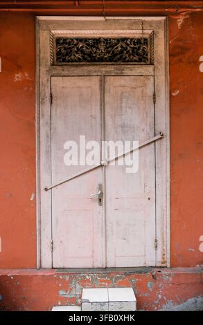 Vintage off-white wooden door with diagonal metal bar lock and carved transom Stock Photo