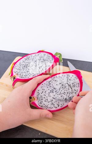 Person holding fresh cut dragon fruit half and eating sweet white pulp with a metal spoon, close up of healthy organic tropical pitaya snack Stock Photo