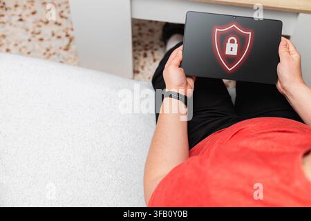 Person using tablet displaying shield and lock icon, symbolizing digital data protection and privacy Stock Photo