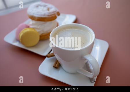 High angle view of cozy coffee break with cup of cappuccino, colorful French macarons and sweet meringue cookies on rustic white wooden table Stock Photo
