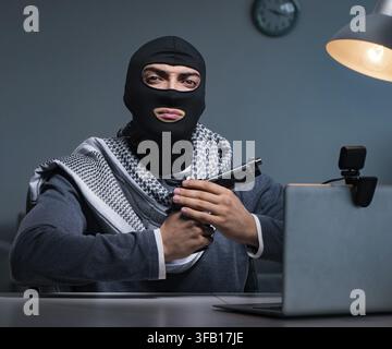 The terrorist burglar with a weapon works on a computer Stock Photo