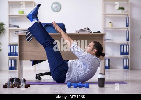Handsome male employee doing exercises in office Stock Photo