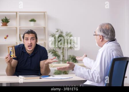 Young male patient visits elderly doctor in time management concept Stock Photo