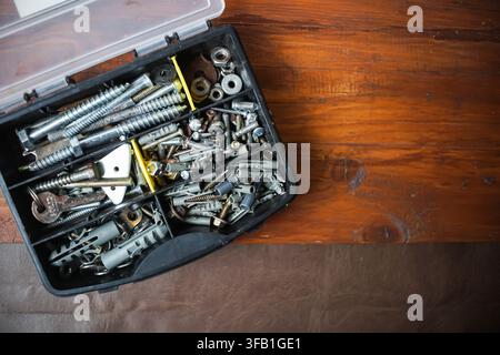 Open plastic organizer filled with assorted screws, bolts, springs, nuts and metal hardware on a rustic wooden table with empty copy space. Stock Photo
