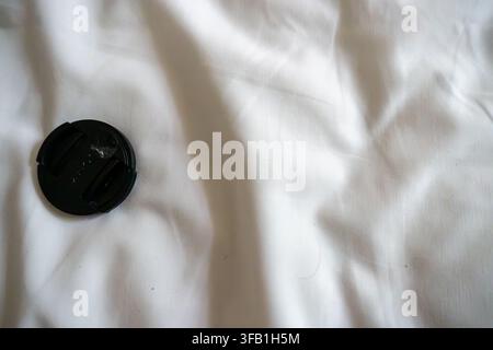 Camera lens cap resting on white fabric surface. Stock Photo