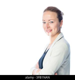 Side profile studio portrait of a blonde businesswoman in a light grey blazer standing with arms crossed, smiling turned toward the camera against a white backdrop Stock Photo