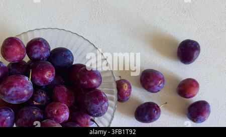 Fresh ripe purple plums presented in a clear glass dish, suitable for food, nutrition, seasonal produce and healthy eating concepts with copy space. Stock Photo