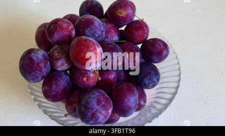 Ripe purple plums arranged in a clear glass bowl, creating a natural seasonal fruit still life with rich color and texture. Stock Photo