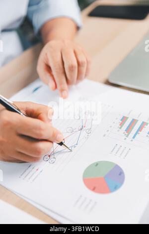 Business professional analyzing a printed line graph with pen beside a laptop, representing data analysis, performance tracking, financial planning, s Stock Photo
