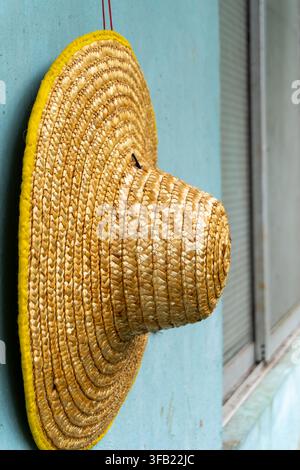 Straw hat hanging on light blue wall exterior. Stock Photo