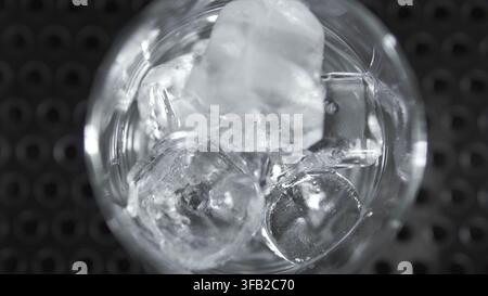 Ice cubes dropping and clinking in a clear glass on a dark background, indicating refreshment and chilling beverages Stock Photo
