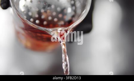 Pouring hot tea infusion from glass teapot with strainer, creating refreshing herbal beverage Stock Photo