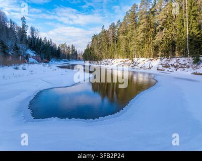 Partly Frozen River Flowing Through Snow Covered Forest in Winter, Latvia Stock Photo