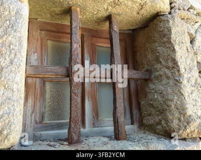 .Antique and rustic wrought iron grille with thick iron bars, installed over a wooden window on the facade of an old stone house in Galicia, Spain. Stock Photo