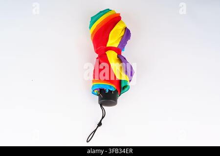 Folded multi-colored rainbow umbrella isolated on a seamless white background, showcasing vibrant colors and compact, portable travel design ideal for Stock Photo