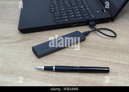 Close-up shot of a modern ribbed grey aluminum external M.2 NVMe SSD enclosure connected via USB-C cable to a black laptop, accompanied by an elegant Stock Photo