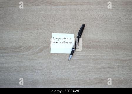 Close-up of a yellow adhesive sticky note with login credentials and a password written on it, attached to a black notebook on a wooden office desk. L Stock Photo