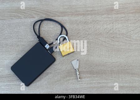 Close-up view of a small brass padlock physically secured around the USB cable of a black external hard drive. Laptop keyboard visible on the side. Co Stock Photo