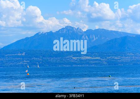 Beautiful blue waters of Lake Geneva feature distant sailboats against a dramatic mountain backdrop of the majestic French Alps on a clear, sunny summ Stock Photo