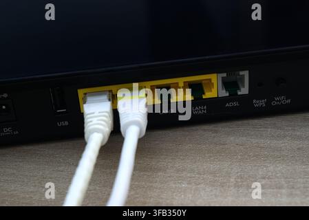 Close-up macro photograph of white ethernet cables connected to a router's LAN ports on a wooden surface. Concept of network infrastructure, technical Stock Photo