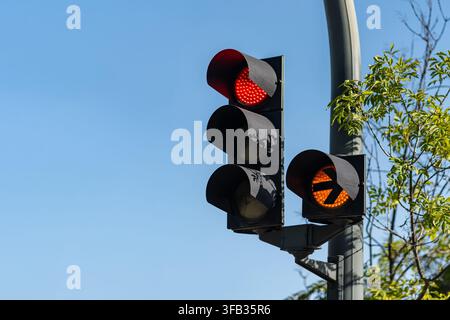 Red stoplight and amber directional arrow signal mounted on a pole against clear blue sky Stock Photo
