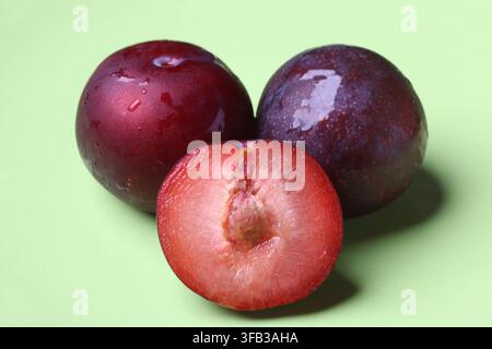 Fresh Red Plums Whole and Half Cut on Green Surface Stock Photo