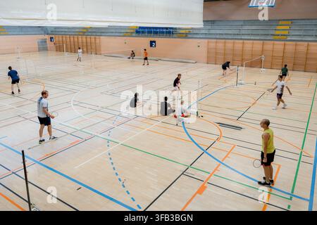 High angle view of badminton tournament players competing on multiple courts inside a spacious indoor sports hall, with nets, rackets, shuttlecocks an Stock Photo