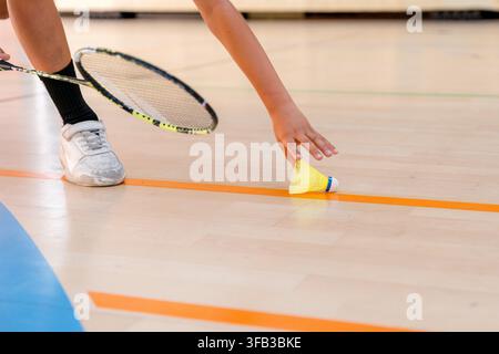 Close-up detail of a badminton player retrieving a shuttlecock beside a racket on an indoor court during a tournament, showing athletic footwear, cour Stock Photo