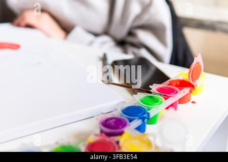 Close-up of colorful paint cups, brushes, and a white palette on a table, suggesting a creative home art project, DIY decoration, and relaxed lifestyl Stock Photo