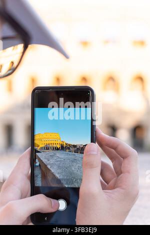 Close-up of a tourist using a smartphone to photograph the illuminated Colosseum in Rome, Italy, capturing an iconic ancient landmark during a city tr Stock Photo
