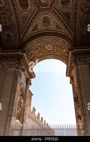 Upward view through an ornate carved archway at St. Peter's Basilica in Vatican City, revealing classical columns, sculpted saints, decorative ceiling Stock Photo