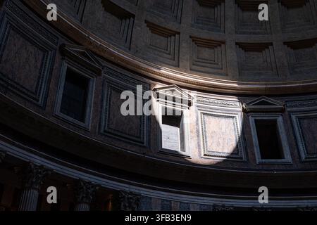 Dramatic sunlight enters the ancient Pantheon in Rome, Italy, illuminating ornate marble wall panels, classical columns, and the monumental curved int Stock Photo