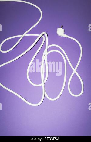 White electrical cord with a two-prong plug arranged in loose loops on a purple background, creating a simple studio still life. Stock Photo