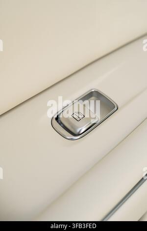 Close-up of an electric car window control button set into a beige interior door panel, highlighting metallic trim, soft leather texture, and modern v Stock Photo